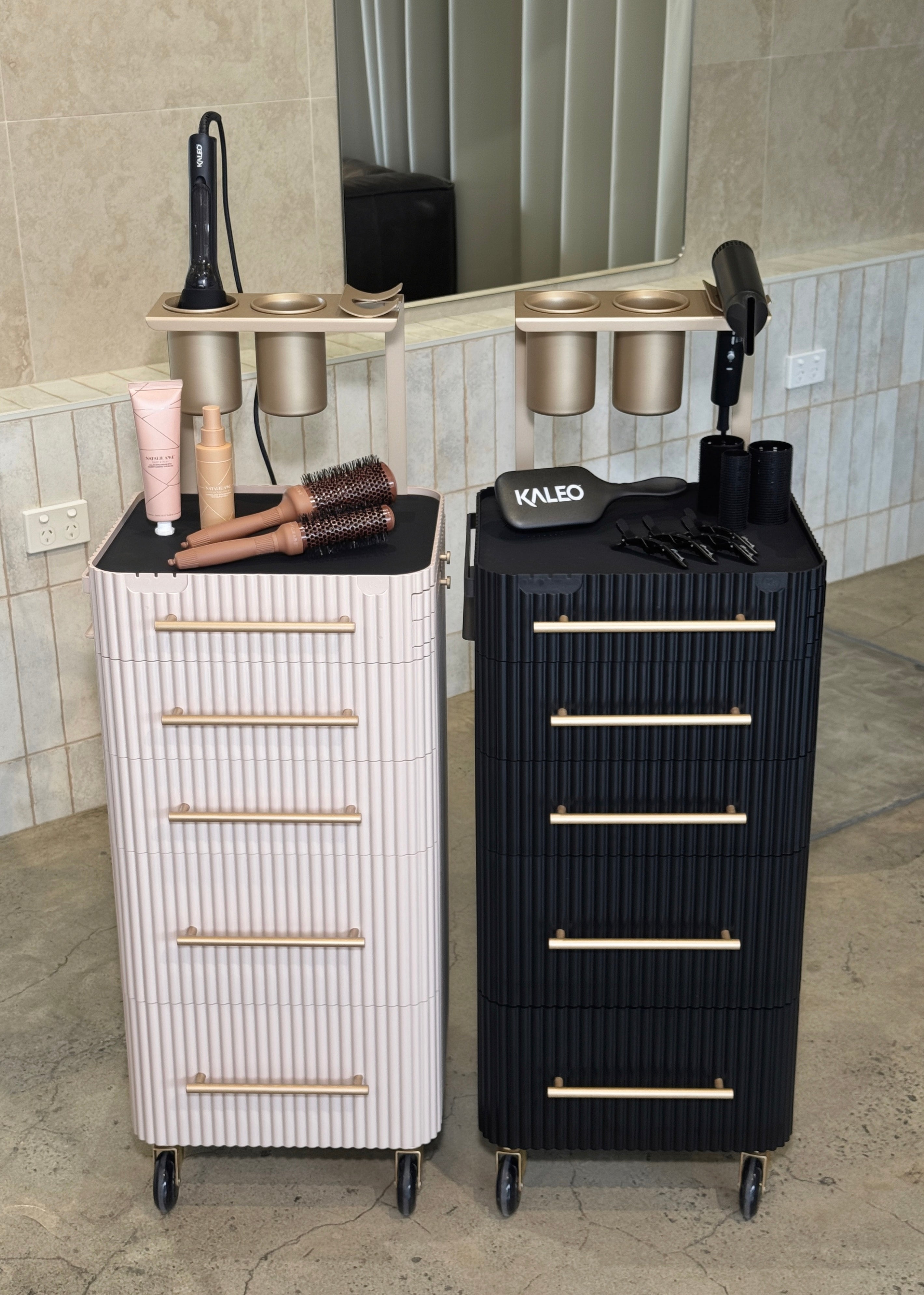 Two salon carts, one white and one black, with hair tools on a tiled floor.